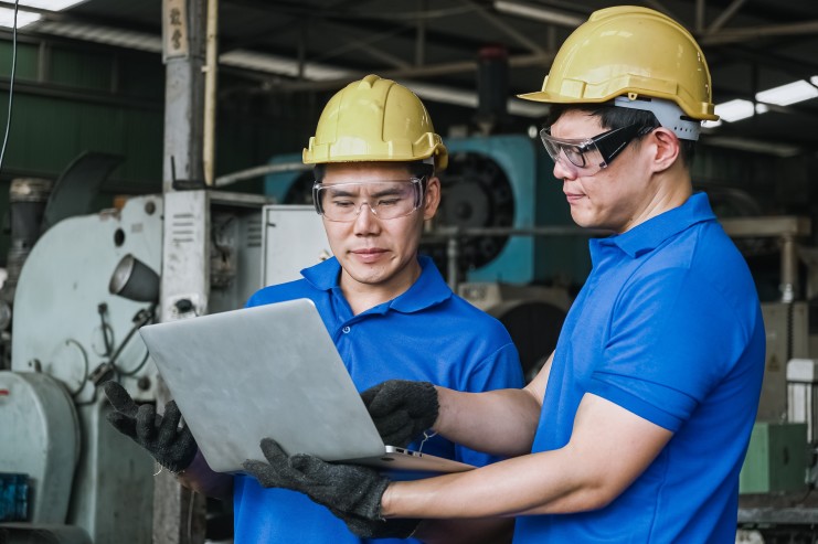 two men in hard hats looking at electronic work instructions on their laptops