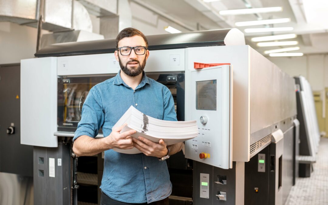 young man holding a stack of paper work instructions infront of a manufacturing machine