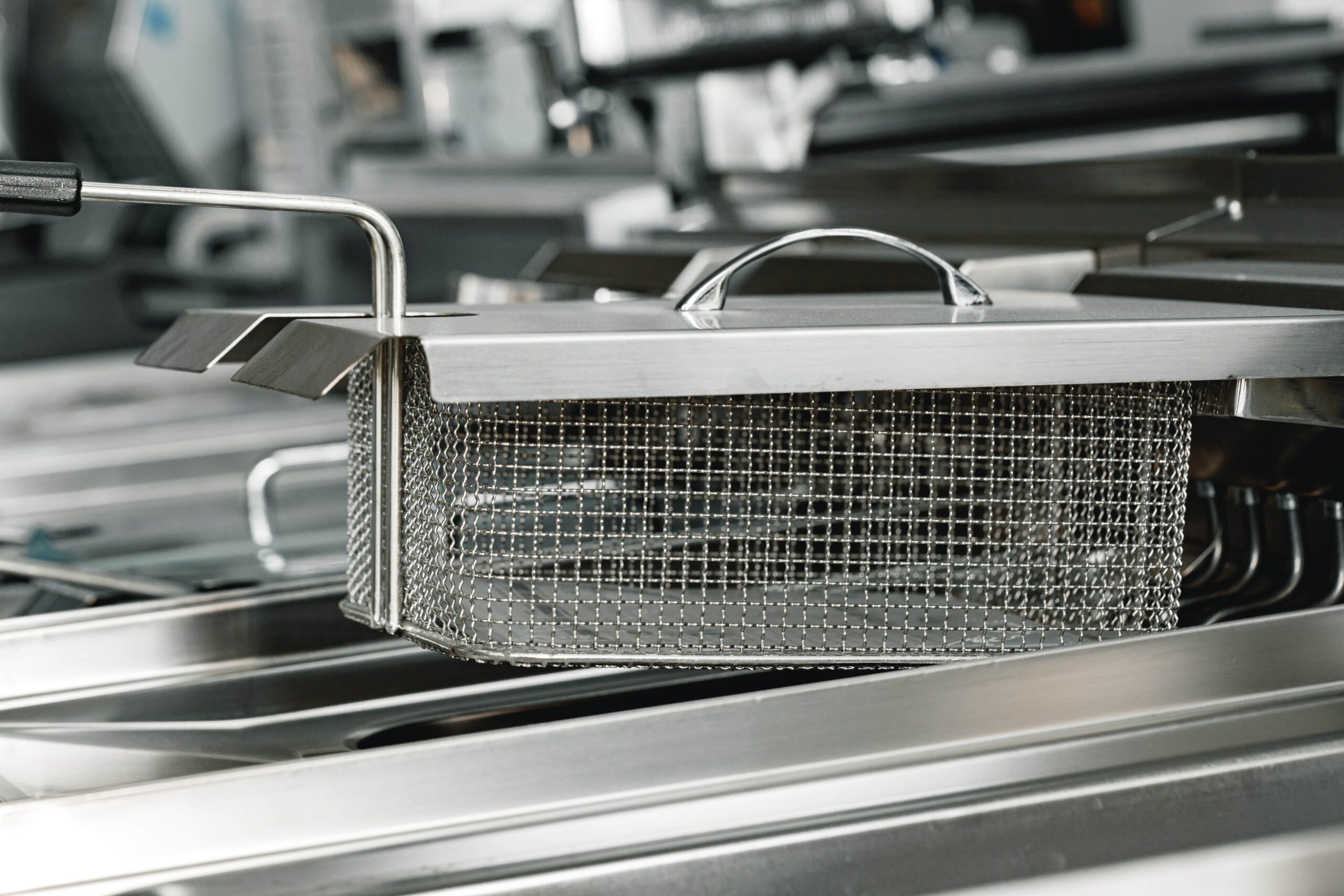 new-industrial-deep-fryer-equipment-close-up-2023-11-27-05-20-31-utc-min up close photo of a food frying basket hovering over a fryer